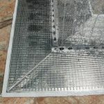 A close-up view of a metal floor grate set into a stone surface, showing water spraying over part of the grate—an ideal moment to consider linear drain maintenance or refer to your strip drain checklist.